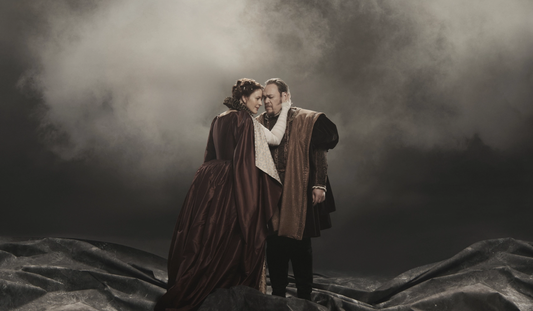 Woman playing Lady Macbeth presses her forehead to forehead of man playing Macbeth on smoky stage at the Met